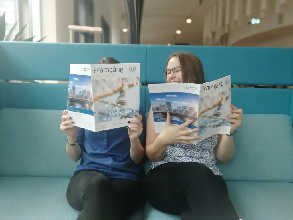 Två tjejer sitter i en turkos soffa och håller varsitt tidningsuppslag framför sig