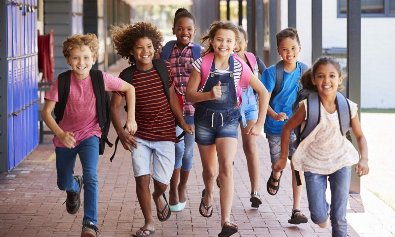 En grupp skolbarn springer på en skolgård dagtid.